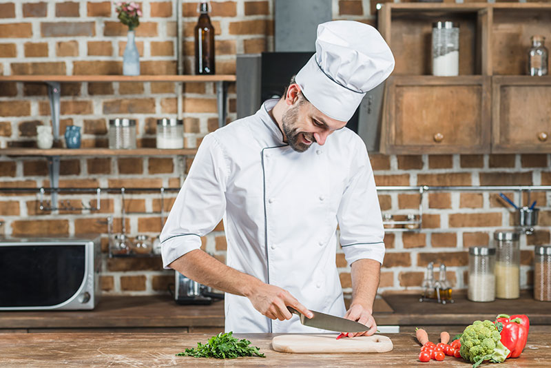 happy-young-male-chef-cutting-red-chili-with-knife-kitchen-counter happy-young-male-chef-cutting-red-chili-with-knife-kitchen-counter